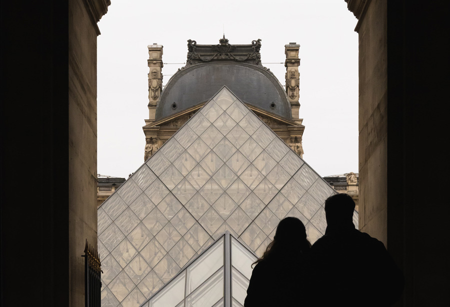 Le Louvre glass pyramid with couple standing outside by Liam McGarry